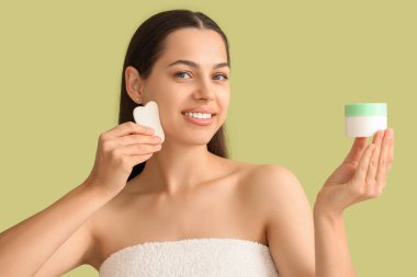 Güzel genç bir kadın yüzüne guasha ve krem sürerek masaj yapıyor.