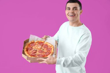 Mor arka planda lezzetli pepperonili pizzalı genç adam.