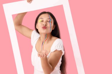 Yüzü boyalı ve çerçevesi pembe arka planda öpüşen genç Asyalı kadın.