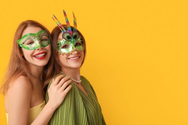 Sarı arka planda, karnaval maskeli mutlu genç kadınlar.