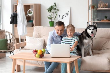 Evde dizüstü bilgisayar kullanan küçük oğlu ve köpeği olan olgun bir doktor.