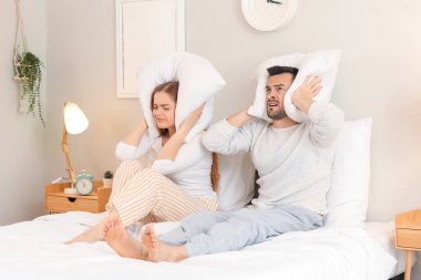 Yatak odasındaki gürültücü komşulardan muzdarip yastıklı genç bir çift.