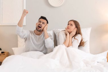 Young couple suffering from loud neighbours in bedroom clipart