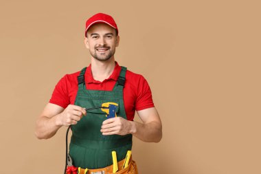 Portrait of male electrician with crimper and wire on beige background clipart