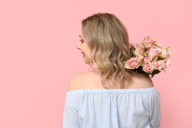 Pembe arka planda bir buket güzel gülleri olan güzel genç bir kadın.