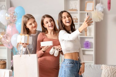 Arkadaşları ve hediyeleriyle genç hamile kadın bebek partisinde selfie çekiyor.