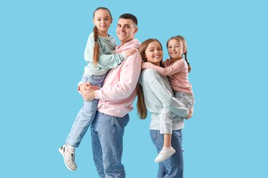 Mavi arka planda küçük kızları olan mutlu bir aile.