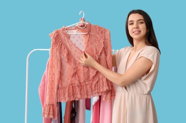 Mavi arka planda elbise askısı olan mutlu kadın stilisti.