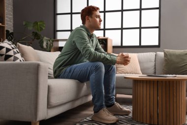 Genç adam evdeki kanepede dua ediyor.