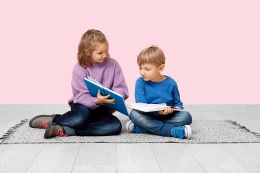Pembe duvarın yanında oturmuş kitap okuyan küçük çocuklar.