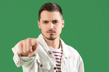 Genç adam yeşil arka plandaki izleyiciyi işaret ediyor, yakın plan. Suçlama kavramı
