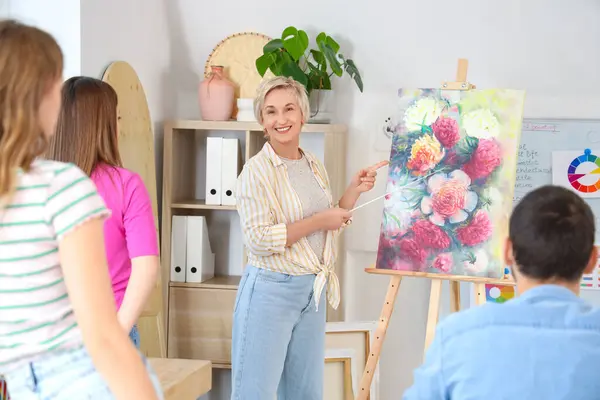Female art teacher with painting giving lecture to students at school