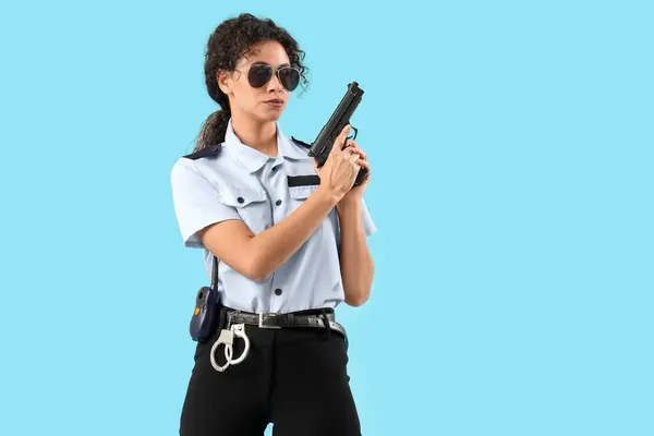 African-American female police officer with gun on blue background