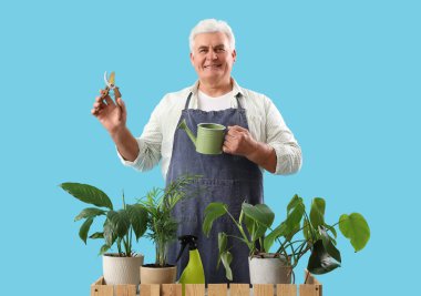 Mezhepçili olgun bahçıvan, sulama kutusu ve mavi arka planda bitkiler.