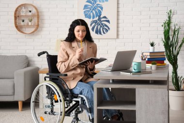 Modern dizüstü bilgisayarıyla tekerlekli sandalyedeki güzel bayan öğrenci ve evde online ders çalışan kitaplar.