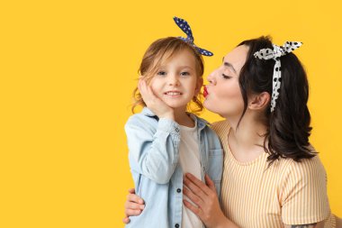 Güzel bir poster kadını sarı arka planda kızını öpüyor.