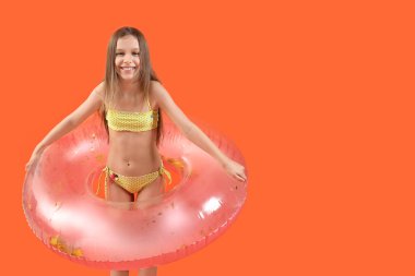 Turuncu arka planda şişirilebilir yüzüğü olan mayo giymiş şirin küçük bir kız.