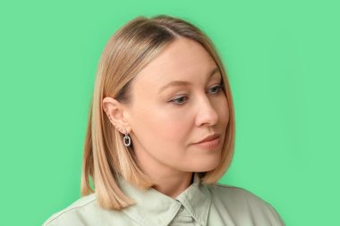 Yeşil arka planda birden fazla kulağı delinmiş bir kadın.