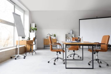 Ekran panosu, masa ve koltukları olan ışık konferans salonu.