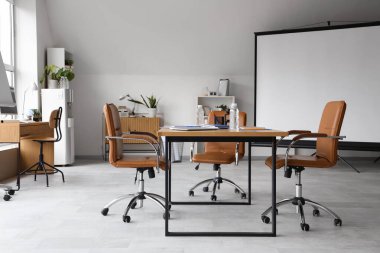 Ekran panosu, masa ve koltukları olan ışık konferans salonu.