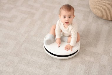Evde robot elektrik süpürgesinin üzerinde oturan şirin bebek.