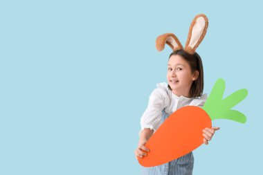 Paskalya tavşanı kulaklı mutlu küçük kız mavi arka planda kağıt havuç