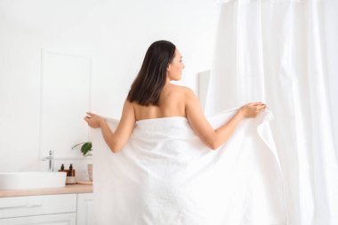 Evinde küvetin yanında havluyla gezen genç bir kadın.