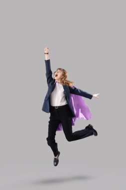 Süper kahraman, komik iş kadını, gri arka plana atlıyor.