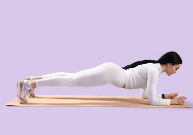 Leylak arka planıyla yoga minderinde pilates yapan genç bir kadının portresi.