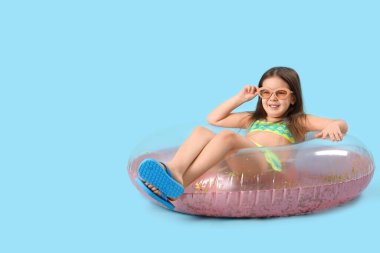 Mavi arka planda şişme yüzüğü olan şirin küçük kız.