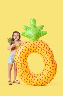 Sarı arka planda ananas şeklinde şişirilebilir halkası olan şirin küçük kız.