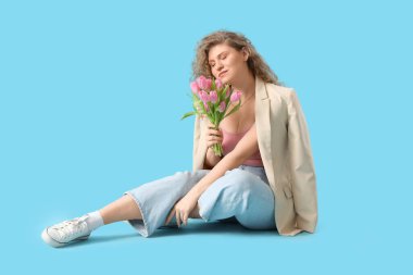 Mavi arka planda oturan güzel lalelerle dolu buketi olan güzel genç bir kadın.