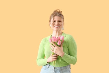 Sarı arka planda güzel pembe lalelerle dolu buketi olan güzel genç bir kadın.