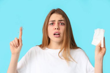 Mavi arka planda toz ve doku alerjisi olan genç bir kadın.