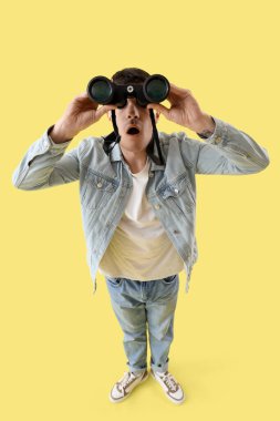 Sarı arka planda dürbünle bakan şok olmuş genç bir adam.