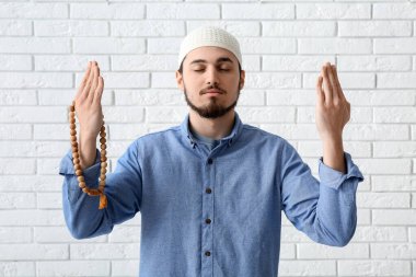 Tasbih 'li genç Müslüman adam beyaz tuğla arka planda dua ediyor.