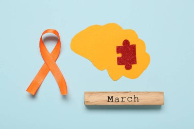 Yapboz parçalı kağıt beyin, mavi arka planda marş ve turuncu kurdele. Çoklu Skleroz Farkındalık Ayı