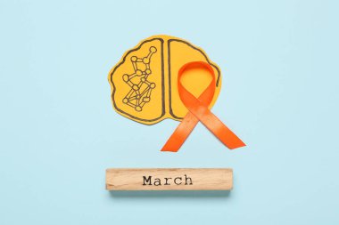 Kelime dağarcığıyla kağıt beyin ve mavi arka planda turuncu kurdele. Çoklu Skleroz Farkındalık Ayı