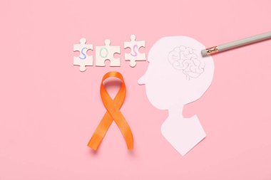 Kağıt üzerinde SOS kelimesi, turuncu kurdele ve pembe arka planda yapboz parçaları olan insan kafası. Çoklu Skleroz Farkındalık Ayı