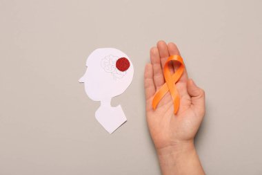Turuncu kurdeleli kadın el ve gri arka planda kağıt insan kafası. Çoklu Skleroz Farkındalık Ayı