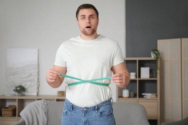 Şok olmuş genç bir adam belini evde ölçüyor. Kilo verme konsepti