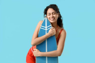 Mavi arka planda sörf tahtası olan güzel, mutlu, Afro-Amerikan bayan cankurtaran.