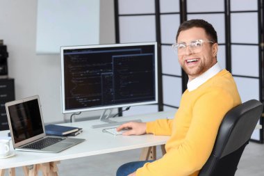 Ofiste bilgisayar ve dizüstü bilgisayarla çalışan erkek programcının portresi
