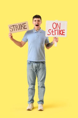 Sarı arka planda pankartlı genç adam protesto ediyor. Grev konsepti