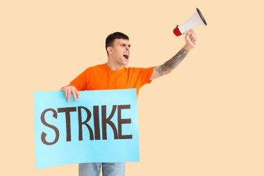 Kelime STRIKE ve bej arka planda megafon ile pankart tutan genç adam protesto ediyor