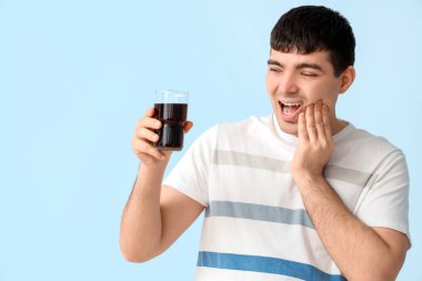 Mavi arka planda diş ağrısından muzdarip bir bardak sodası olan genç adam, yakın plan.