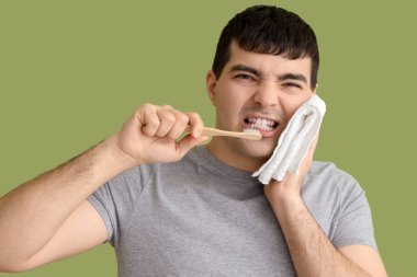 Yeşil arka planda diş ağrısı çeken fırçası ve havlusu olan genç adam, yakın plan.