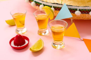 Pembe arka planda tekila ve limon dilimleri, yakın plan.