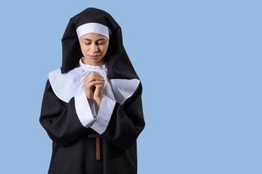 Mavi arka planda dua eden genç bir rahibe