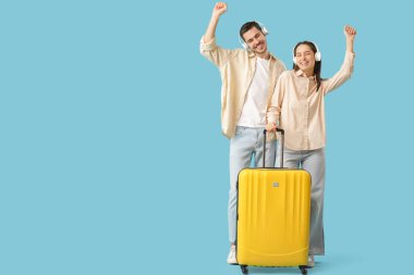 Güzel, genç, mutlu, kulaklıklı, bavullu, mavi arka planda dans eden turistler.